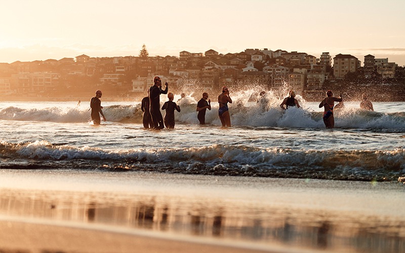 A group of swimmers entering the water at Bondi Beach at dawn