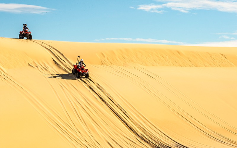 2 people riding four-wheelers down large sand dunes in Port Stephens