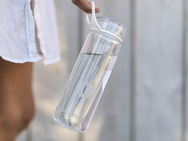 A photograph of a manicured hand holding a clear reusable water bottle 
